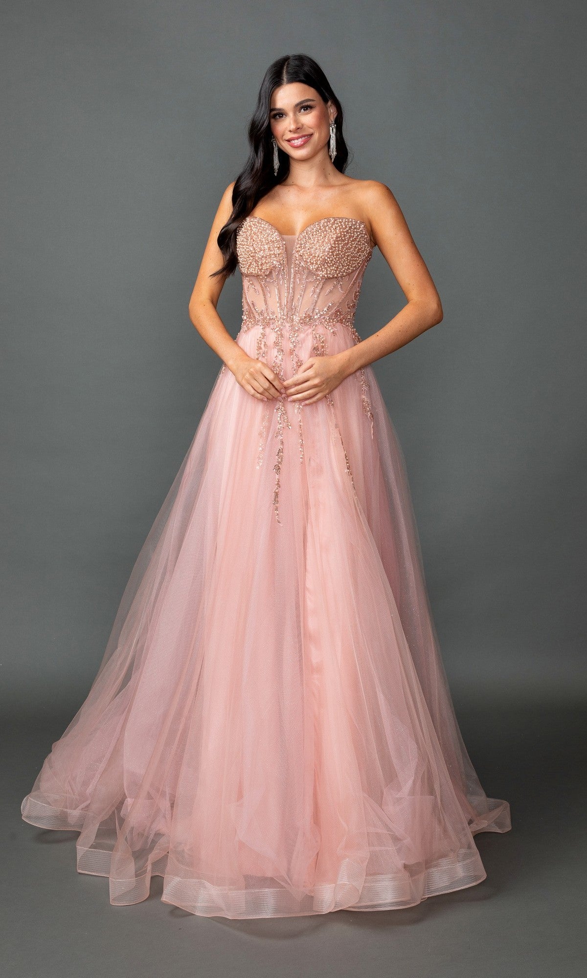 A woman stands against a gray background wearing the Lace-Up Long A-Line Prom Dress: Dancing Queen 4490 in rose gold—a strapless, floor-length gown with an embroidered corset bodice and sheer tulle skirt.